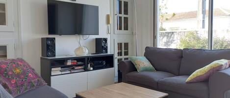 A living room with a flat-screen TV, speakers, a sofa, a coffee table, and a large window.