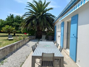 Een terras met een tafel en stoelen, een palmboom en een gebouw met blauwe deuren.