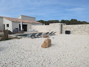 Una casa moderna con piscina, mobiliario exterior y un muro de piedra.