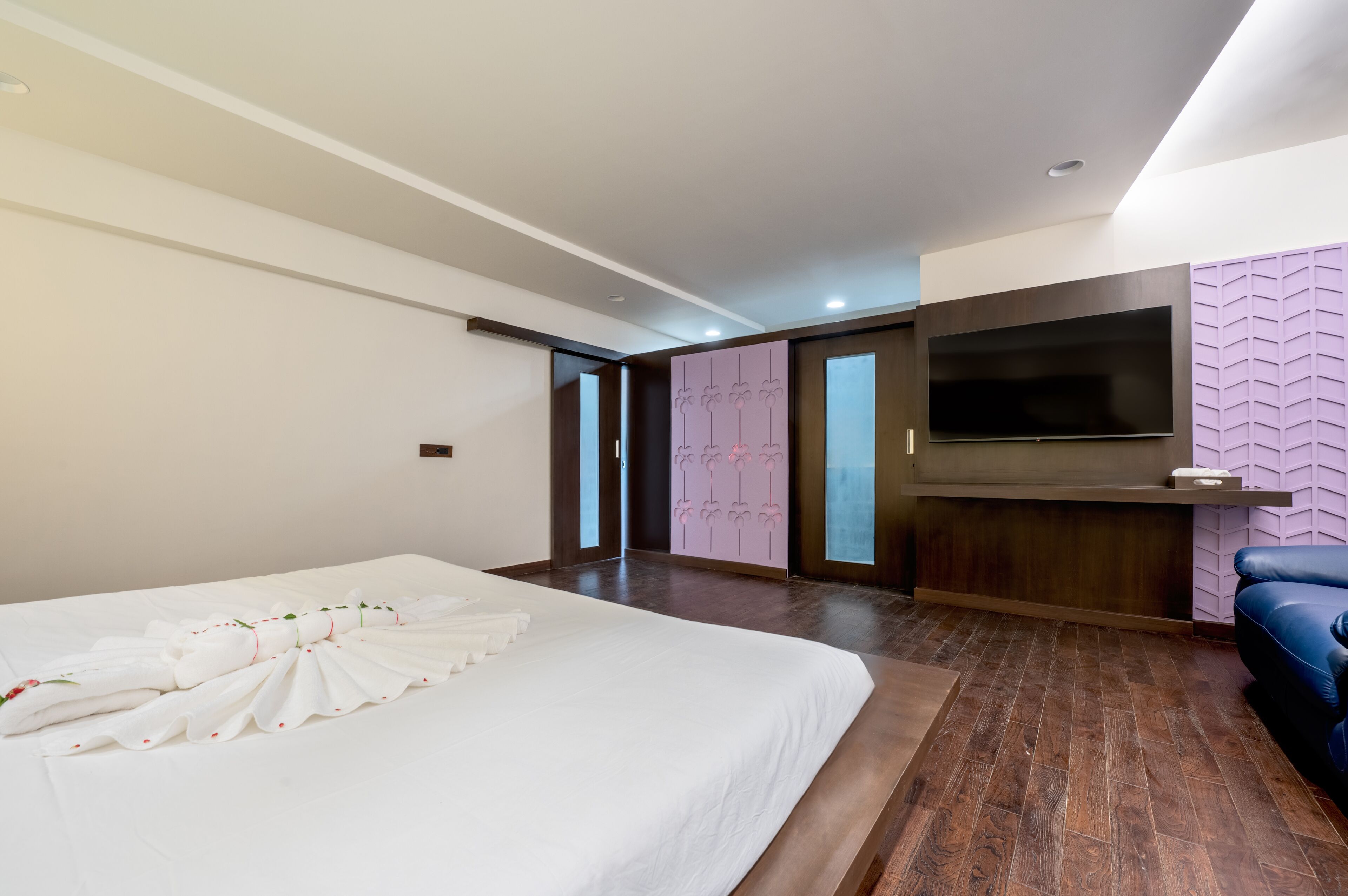 Una habitación de hotel moderna con una cama grande, un televisor de pantalla plana en la pared y un sofá azul.