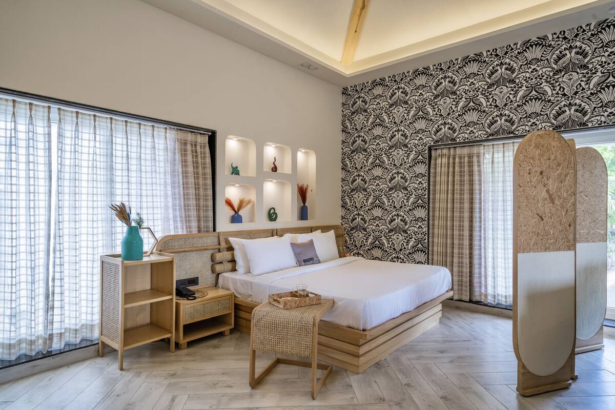 A modern bedroom with a large bed, bedside tables, a nightstand, a decorative wall, and a large window with curtains.