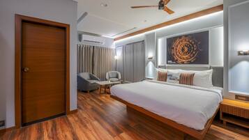 Una habitación de hotel moderna con una cama grande, un ventilador de techo, un área de descanso con una mesa y sillas, y una obra de arte de gran tamaño en la pared.