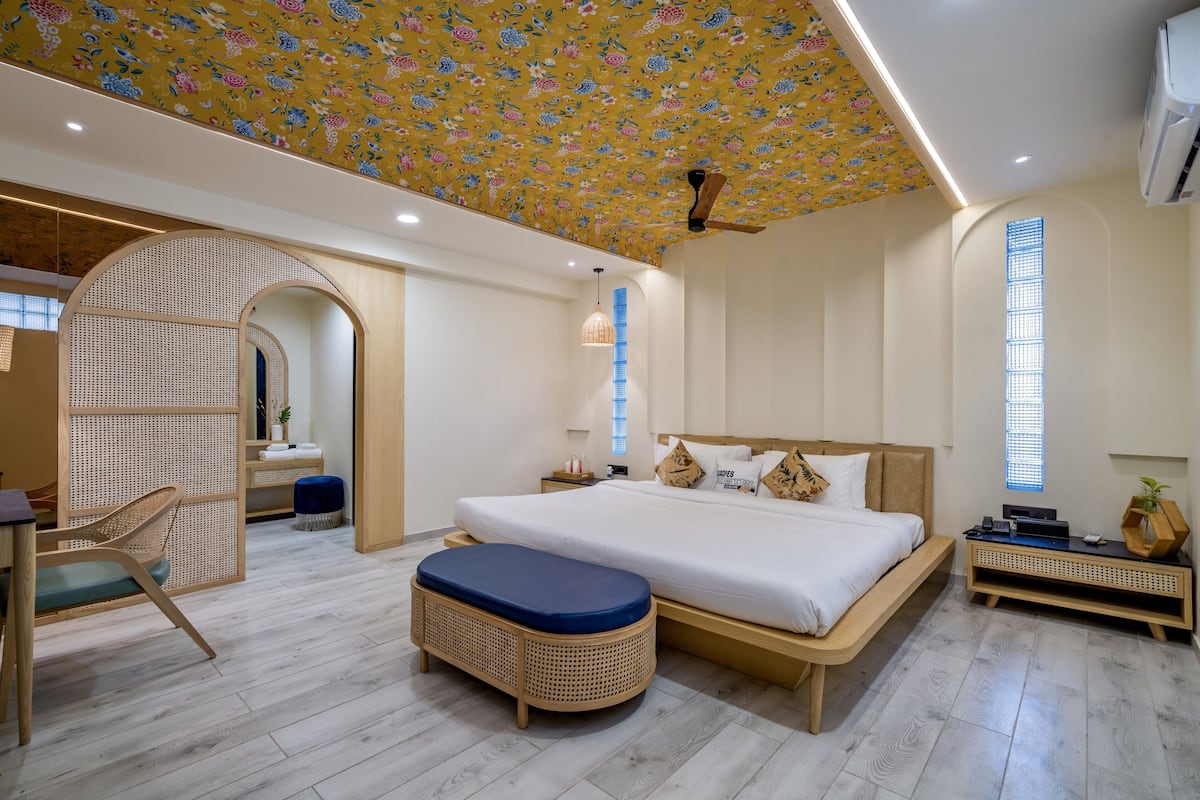 A modern bedroom with a large bed, a wooden bench, a desk, and a ceiling fan.