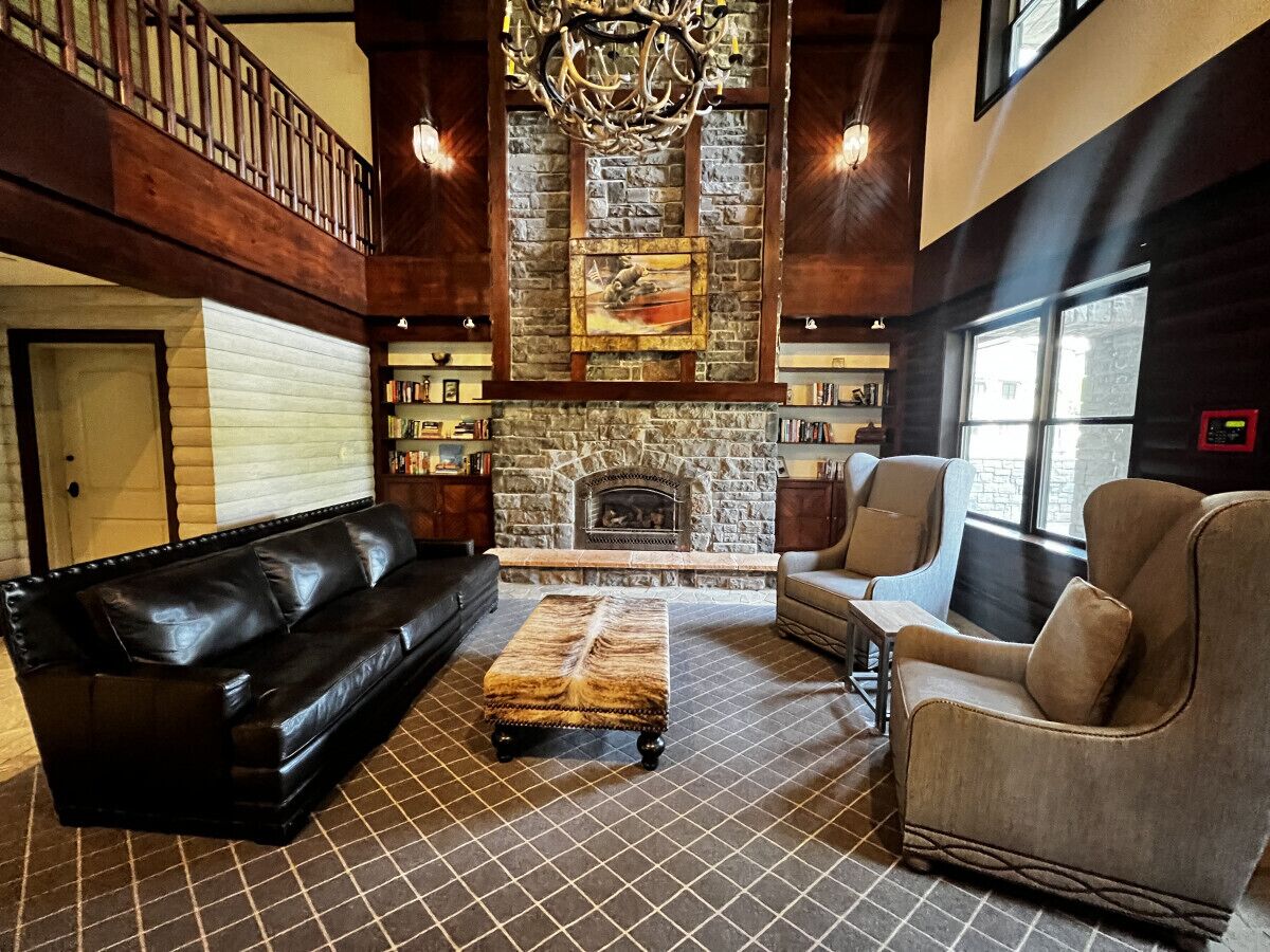 A spacious living room with a fireplace, leather sofa, armchair, and a patterned rug.