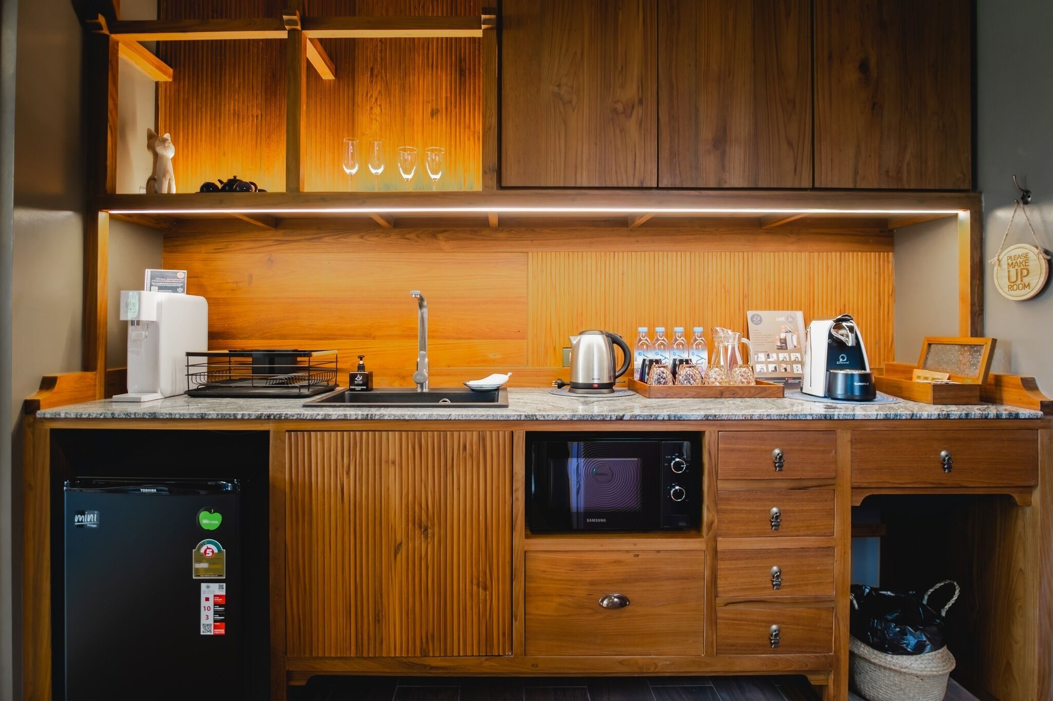 Una cocina moderna con armarios de madera, microondas integrado, cafetera y hervidor.