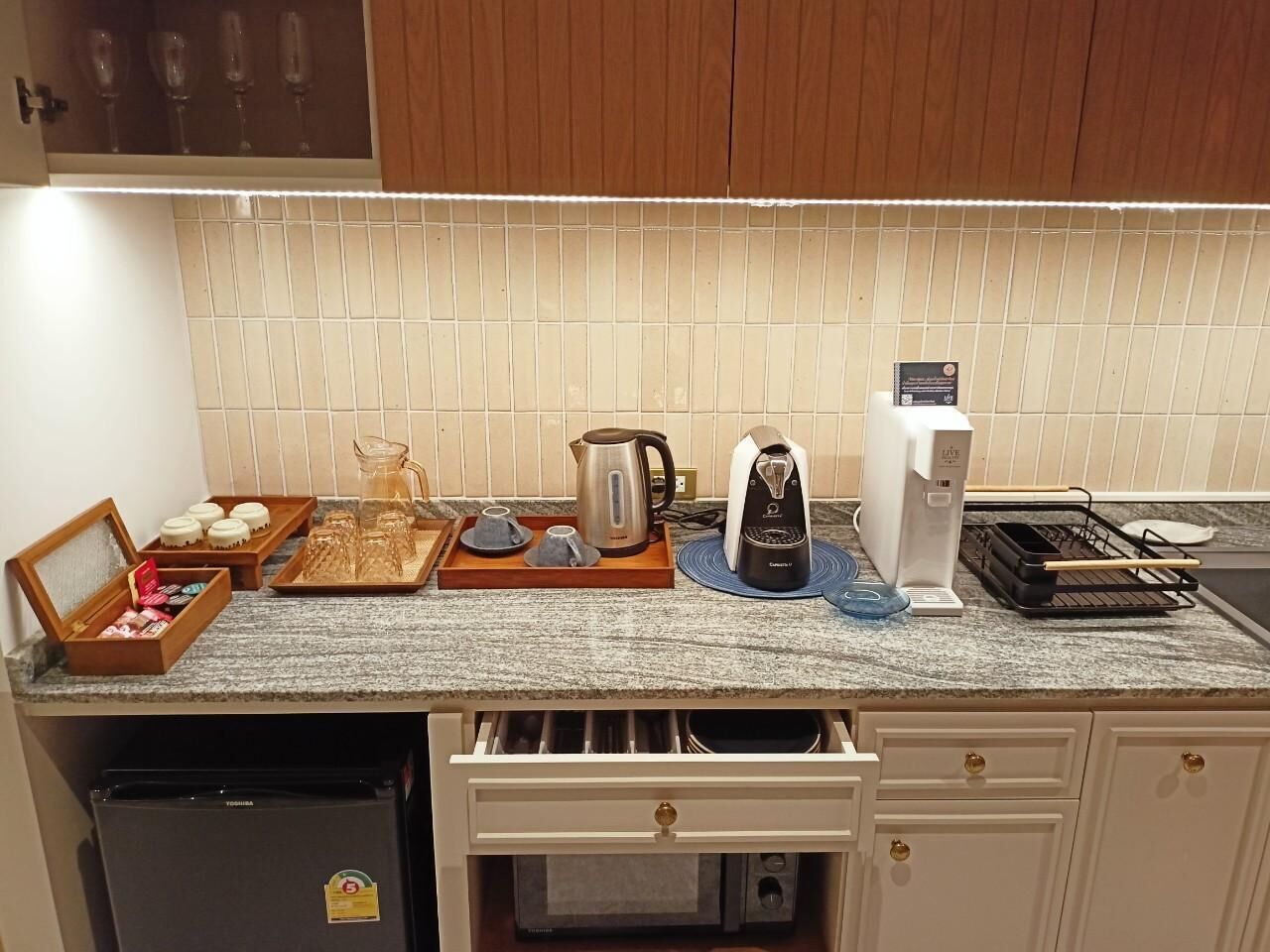 A kitchen with a microwave, coffee maker, kettle, and a toaster. There are also some glassware and a box of chocolates on the counter.
