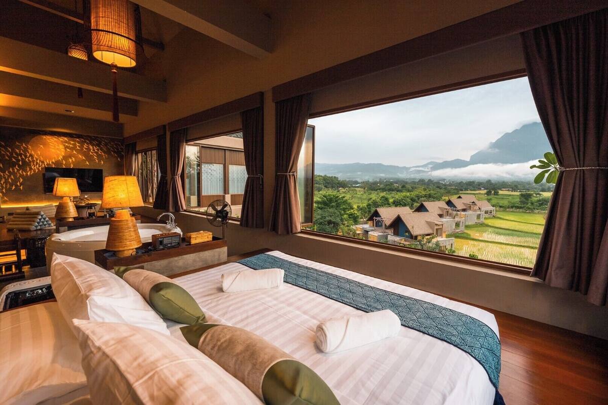 Hotelkamer met een groot bed, een bureau met lamp, een televisie en uitzicht op een dorp en bergen.
