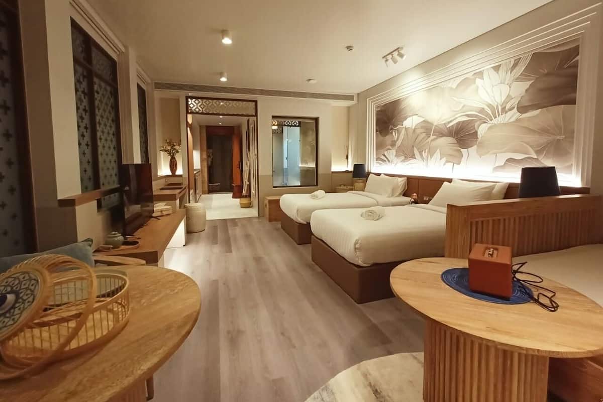 Een hotelkamer met een houten vloer, twee bedden, een zithoek met een houten tafeltje en een kleine houten stoel, plus een grote bloemenmuur.