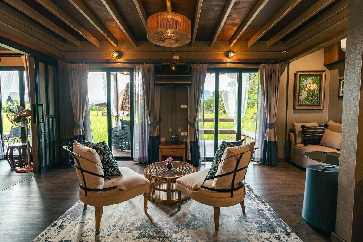 Een ruime zithoek met twee fauteuils, een ronde salontafel en uitzicht op de omgeving via grote schuifdeuren.
