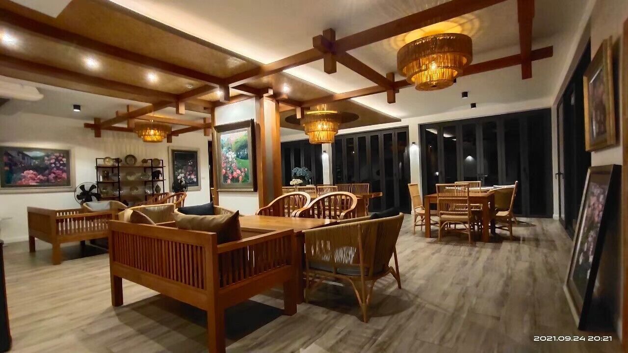 A spacious room with wooden furniture, including a sofa and dining table, and a chandelier.