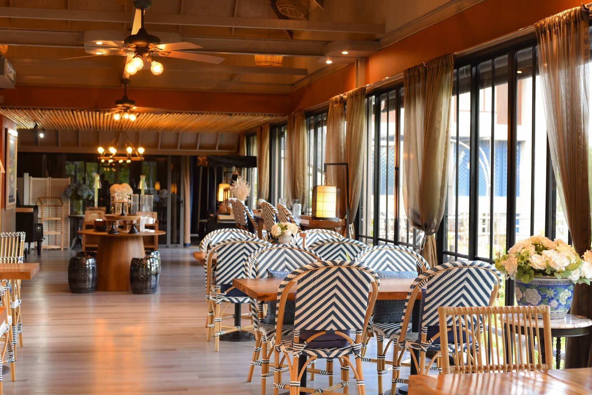 A restaurant with wooden furniture, large windows, and a ceiling fan.