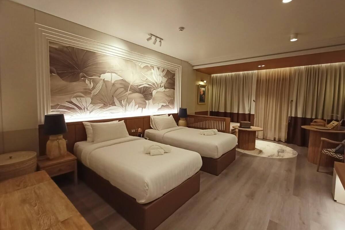 Een hotelkamer met twee bedden, een groot bloemistisch kunstwerk aan de muur, een houten bijzettafeltje, een ronde salontafel en een zithoek met een stoel en een klein tafeltje.