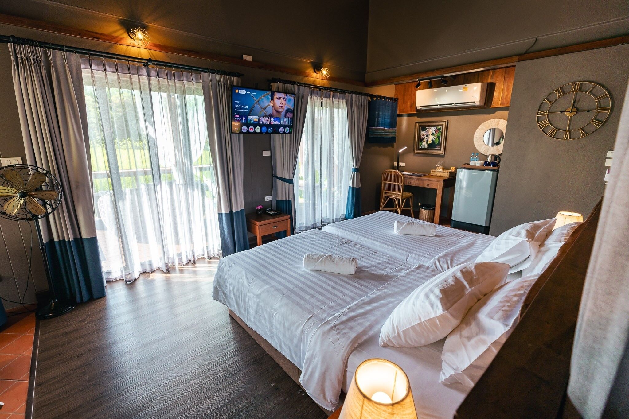 A hotel room with a large bed, a desk, a TV, and a clock on the wall.