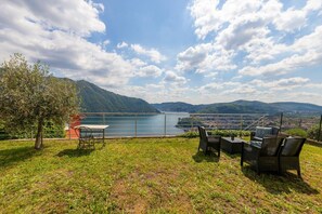 A terrace with outdoor furniture overlooking a lake, surrounded by hills.