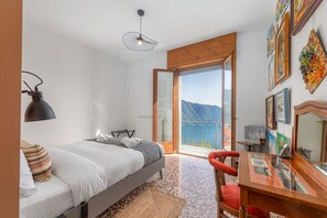 A bedroom with a bed, a desk, and a chair. There is a window with a view of mountains.