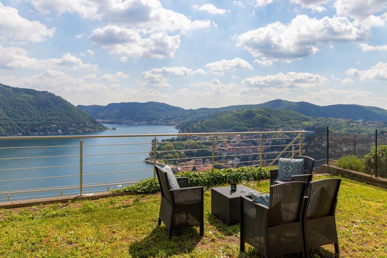 Une terrasse meublée avec des meubles en osier, donnant sur un lac et des collines.