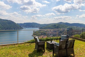 Une terrasse meublée avec des meubles en osier, donnant sur un lac et des collines.