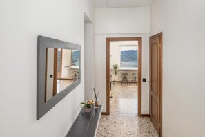 Un couloir avec un miroir, une plante en pot et une vue sur un balcon doté d’une balustrade, avec une montagne en arrière-plan.