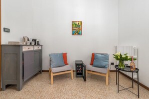 Une petite pièce agréable et chaleureuse, avec deux fauteuils gris dotés de coussins rouges, une petite table sur laquelle est posé un vase de fleurs, un radiateur et un tableau accroché au mur.