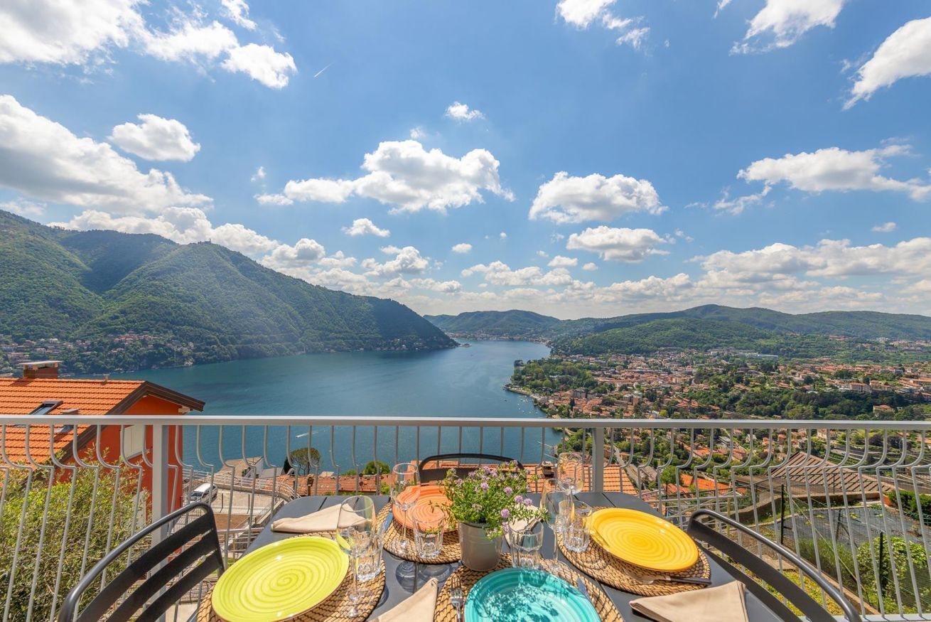 A terrace with a table set for dining, overlooking a lake and mountains.