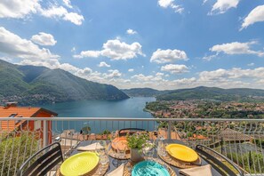A terrace with a table set for dining, overlooking a lake and mountains.
