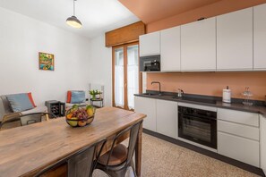 A modern kitchen with white cabinets, a wooden dining table, and a fruit bowl. - Vivi Il Lago - Lake View (Cernobbio)