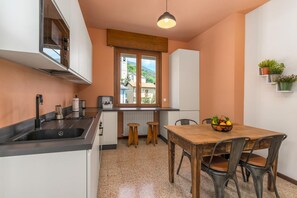A compact kitchen with a sink, stove, and stools. A dining table with chairs is positioned near a window with a view of buildings and greenery. - Vivi Il Lago - Lake View (Cernobbio)