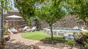 Ein Garten mit Steinmauer, kleinem Baum, Wasserspiel und Liegestühlen.