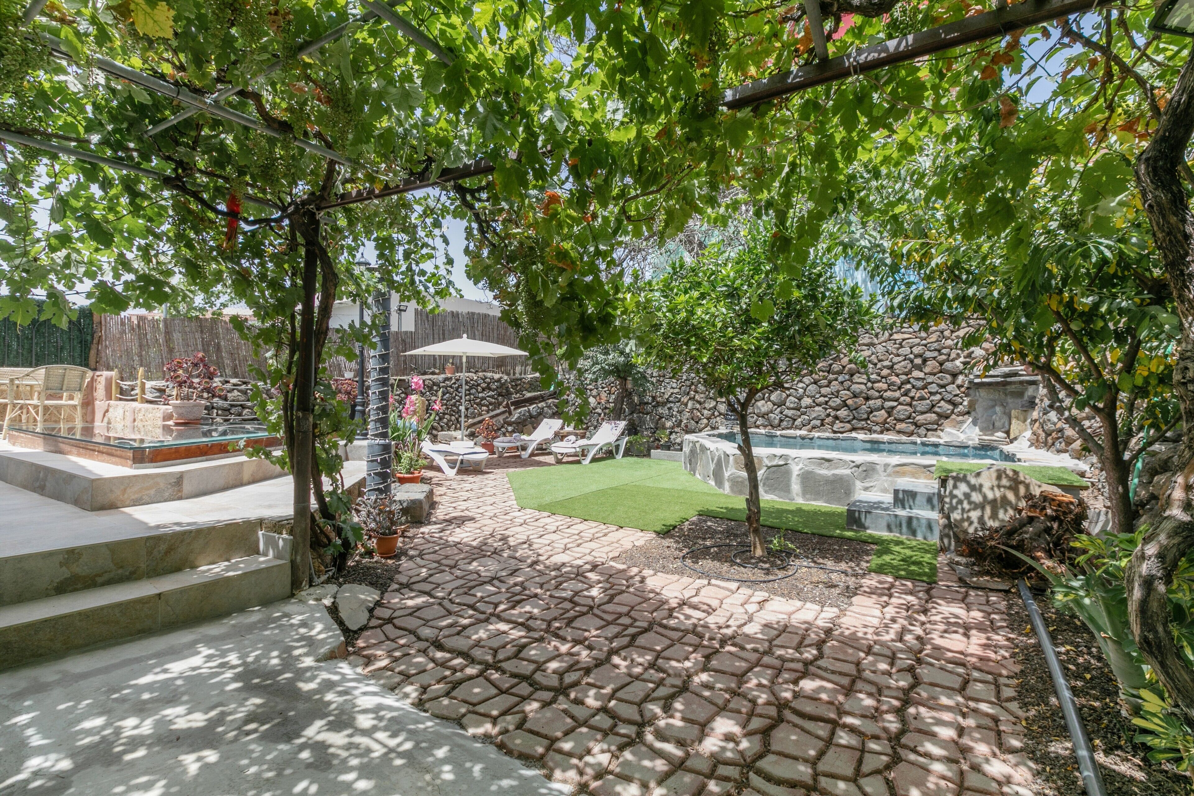 Un patio con baldosas de piedra, una pequeña piscina y sillas de descanso.