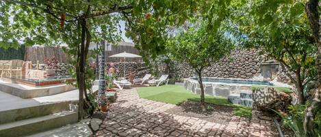 Un patio con baldosas de piedra, una pequeña piscina y sillas de descanso.