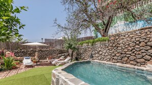 Ein Pool mit Steinmauern, eine Rasenfläche mit Liegestühlen und ein Holzzaun.
