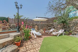 Une terrasse avec un sol en pierre, des fauteuils de jardin blancs, une petite piscine et des plantes en pot.