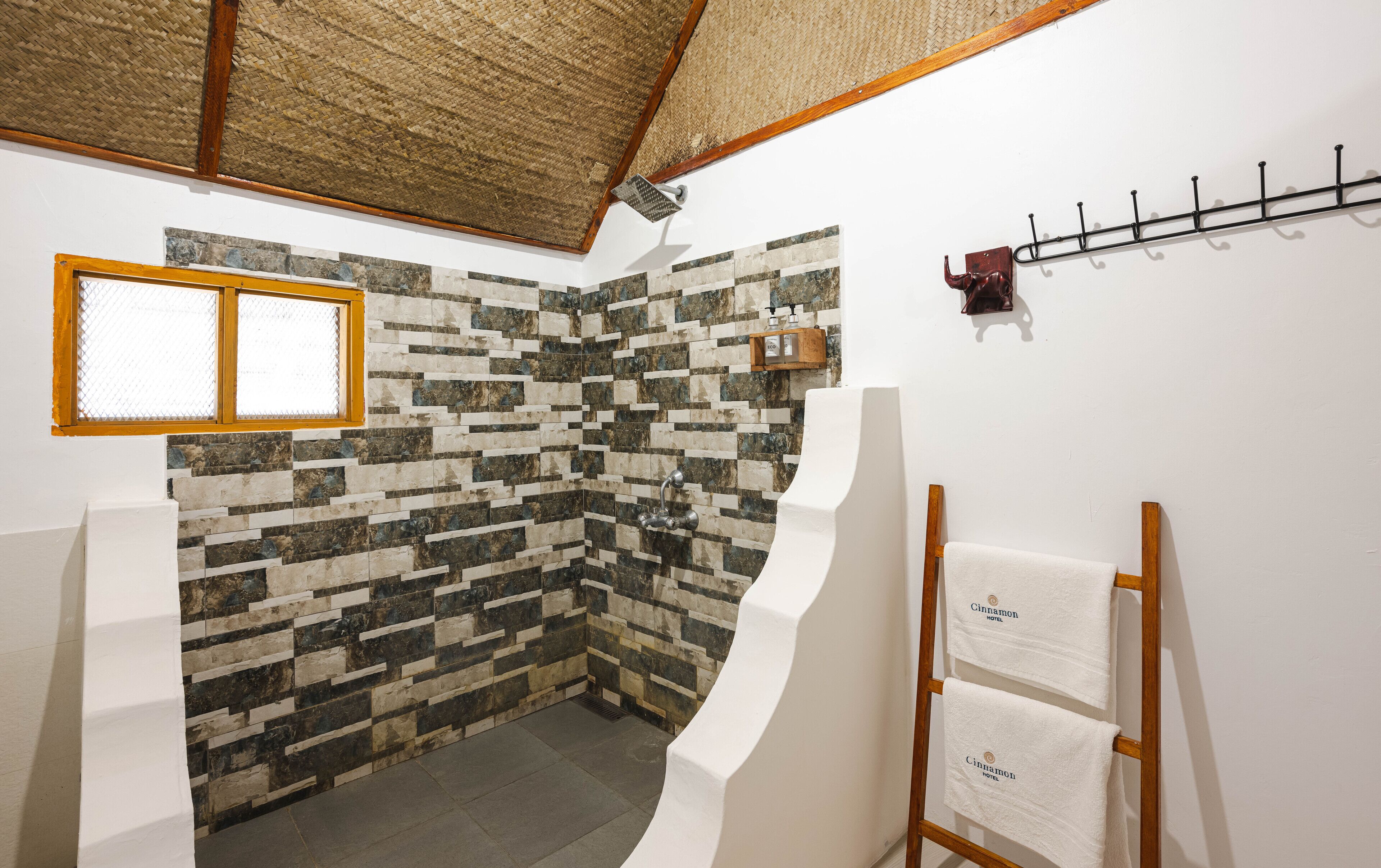 Une salle de bain avec un mur décoré d’une mosaïque de pierre, une échelle en bois sur laquelle sont posées des serviettes et une douche avec un cadre en bois.
