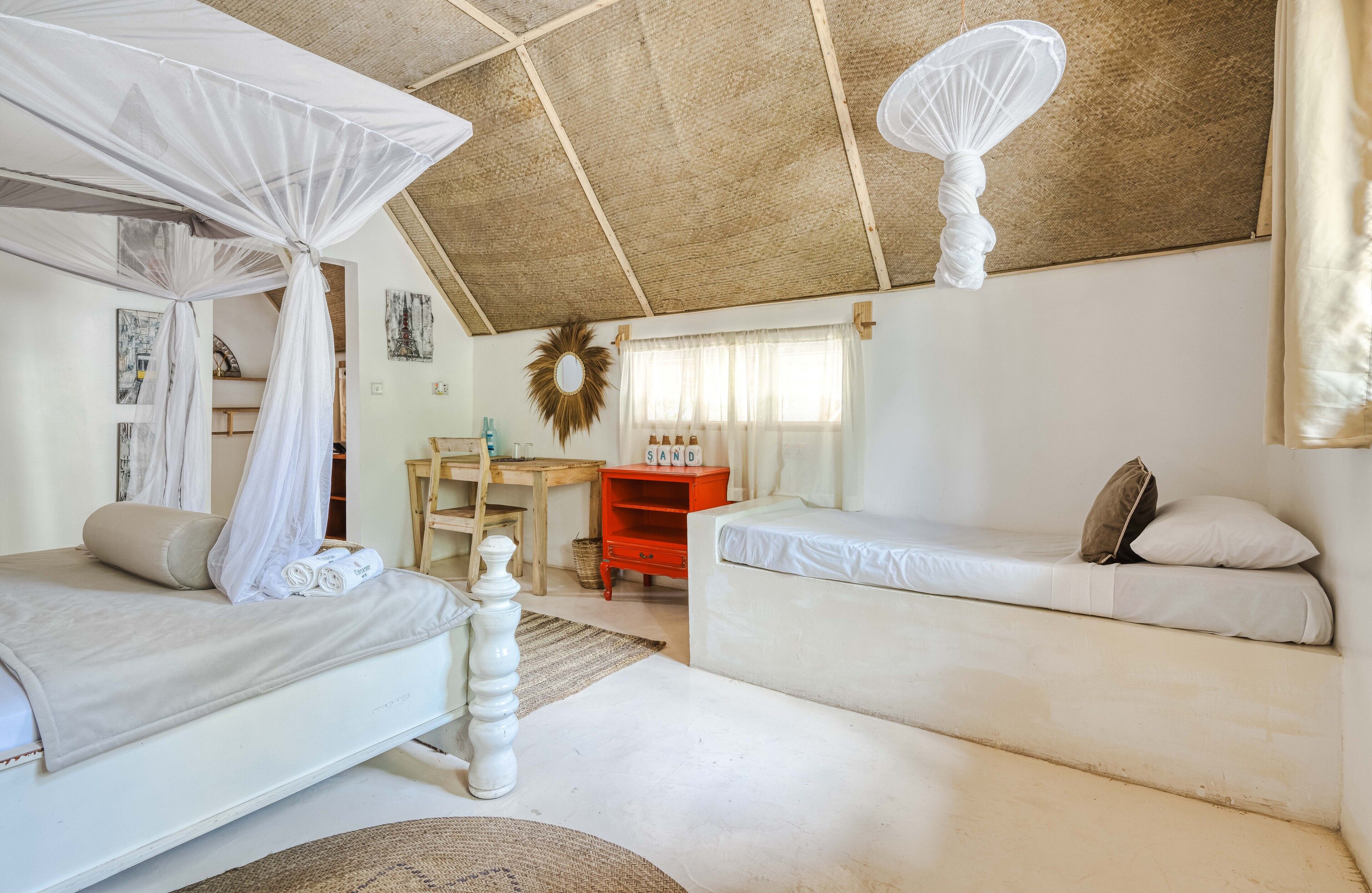 Un dormitorio con cama a dosel, una cama tipo sofá, un escritorio y una silla de mimbre.