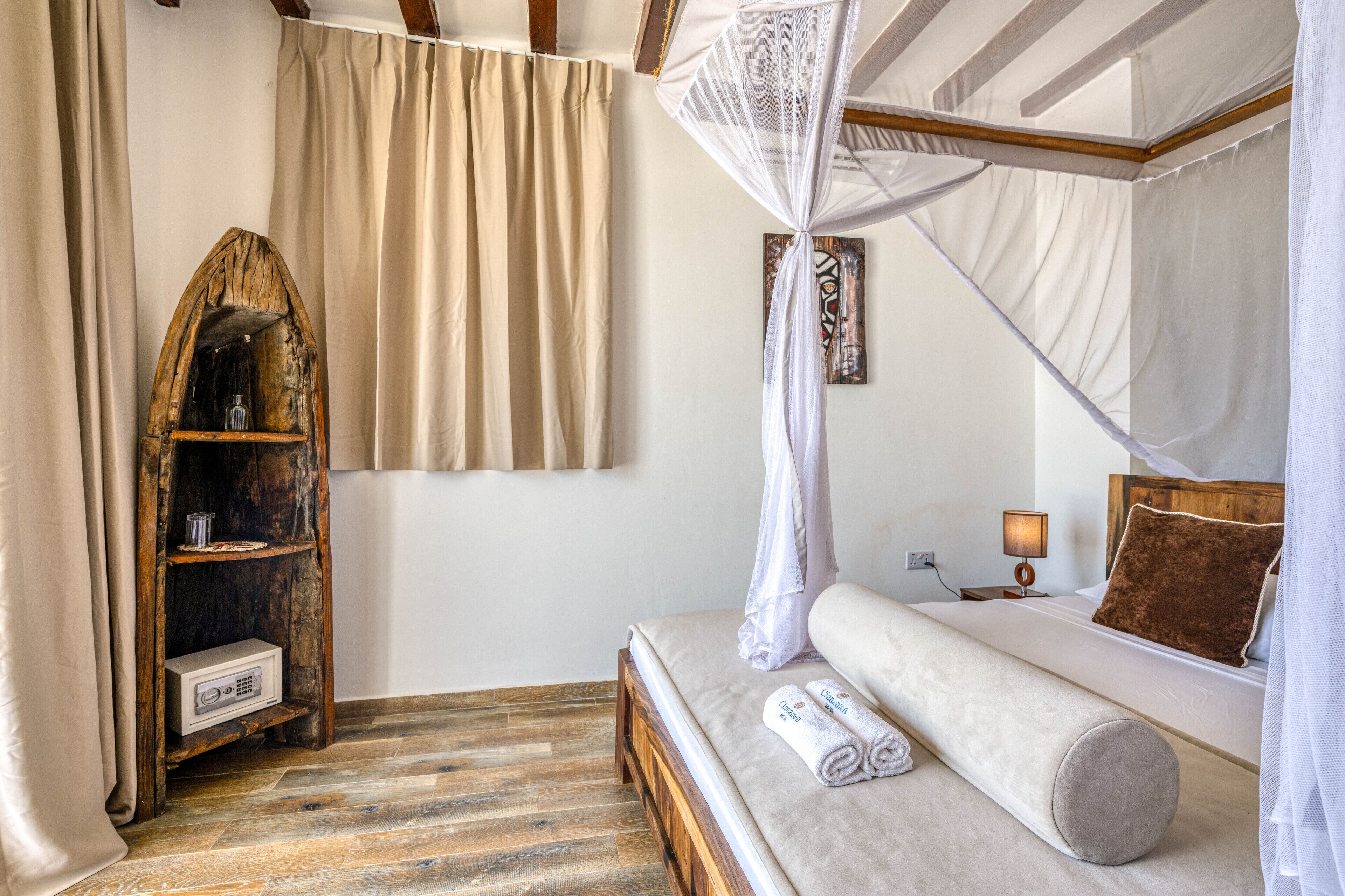 A bedroom with a wooden headboard, a wooden shelf with a glass container, a bedside table with a lamp, and a bed with a white mattress and a brown pillow.