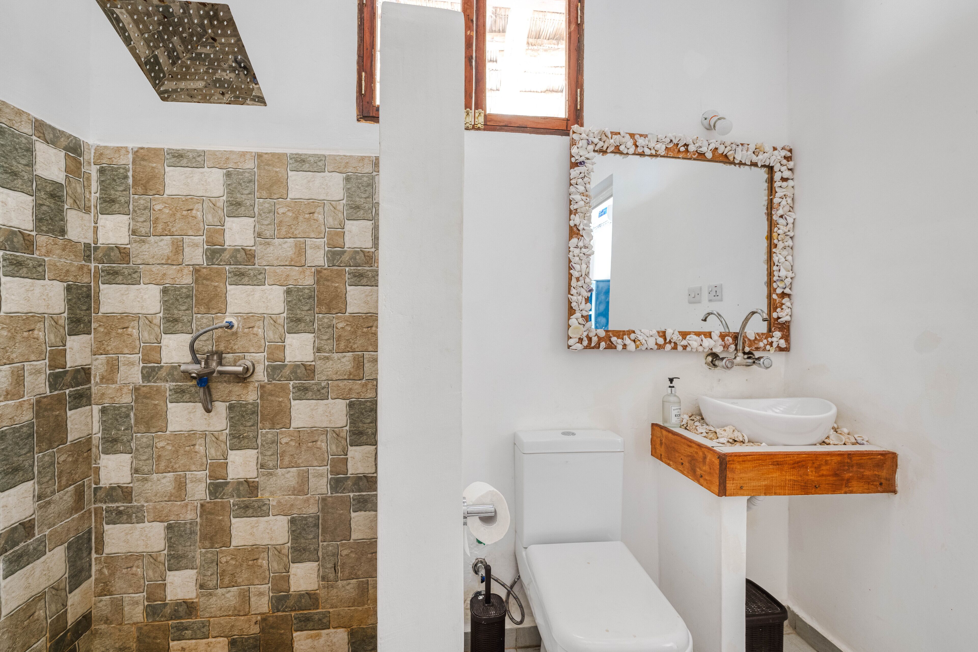 A bathroom with a stone wall, a wooden vanity, a white sink, and a toilet.