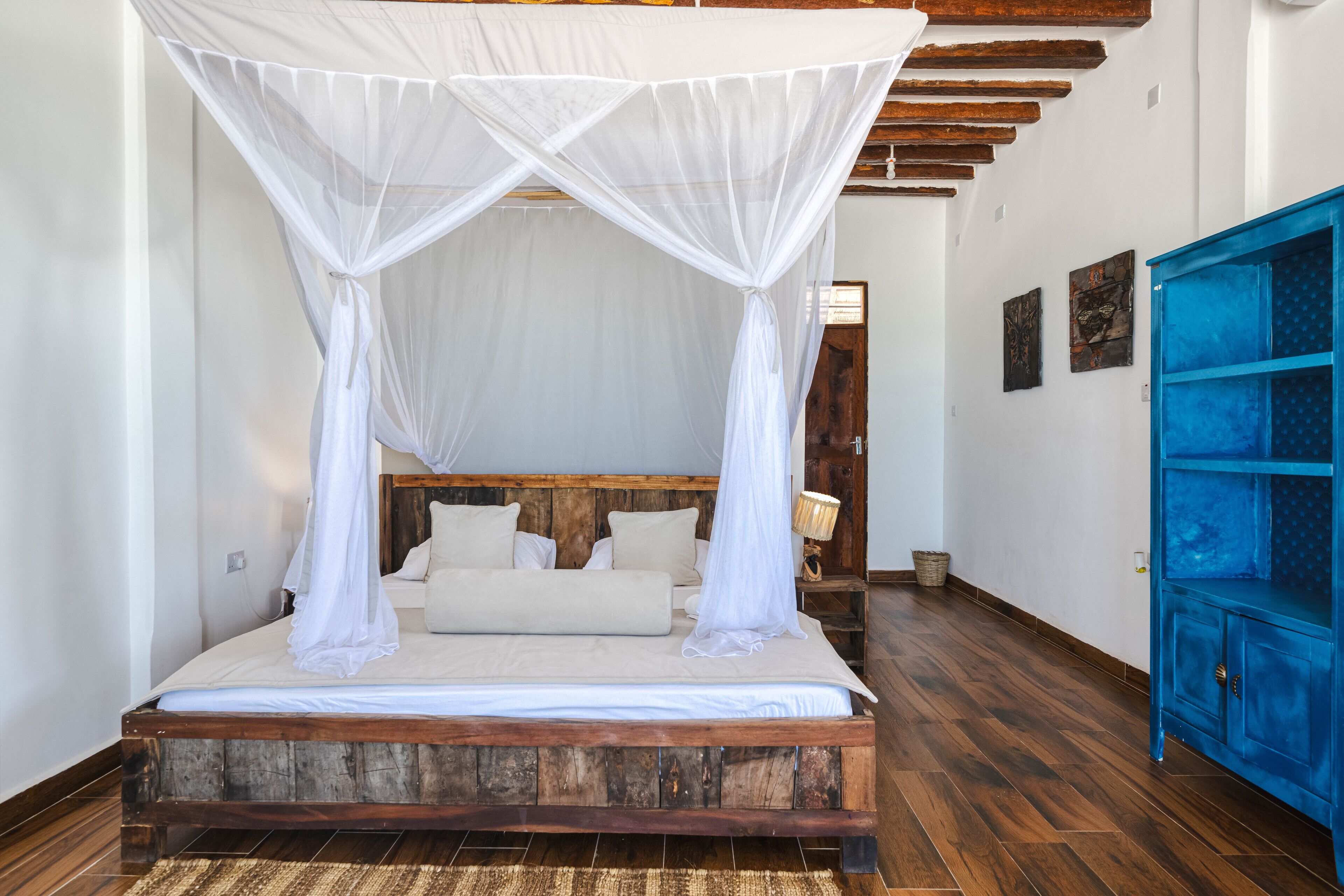 A bed with a wooden frame and white bedding, a blue cabinet, and a wooden floor.