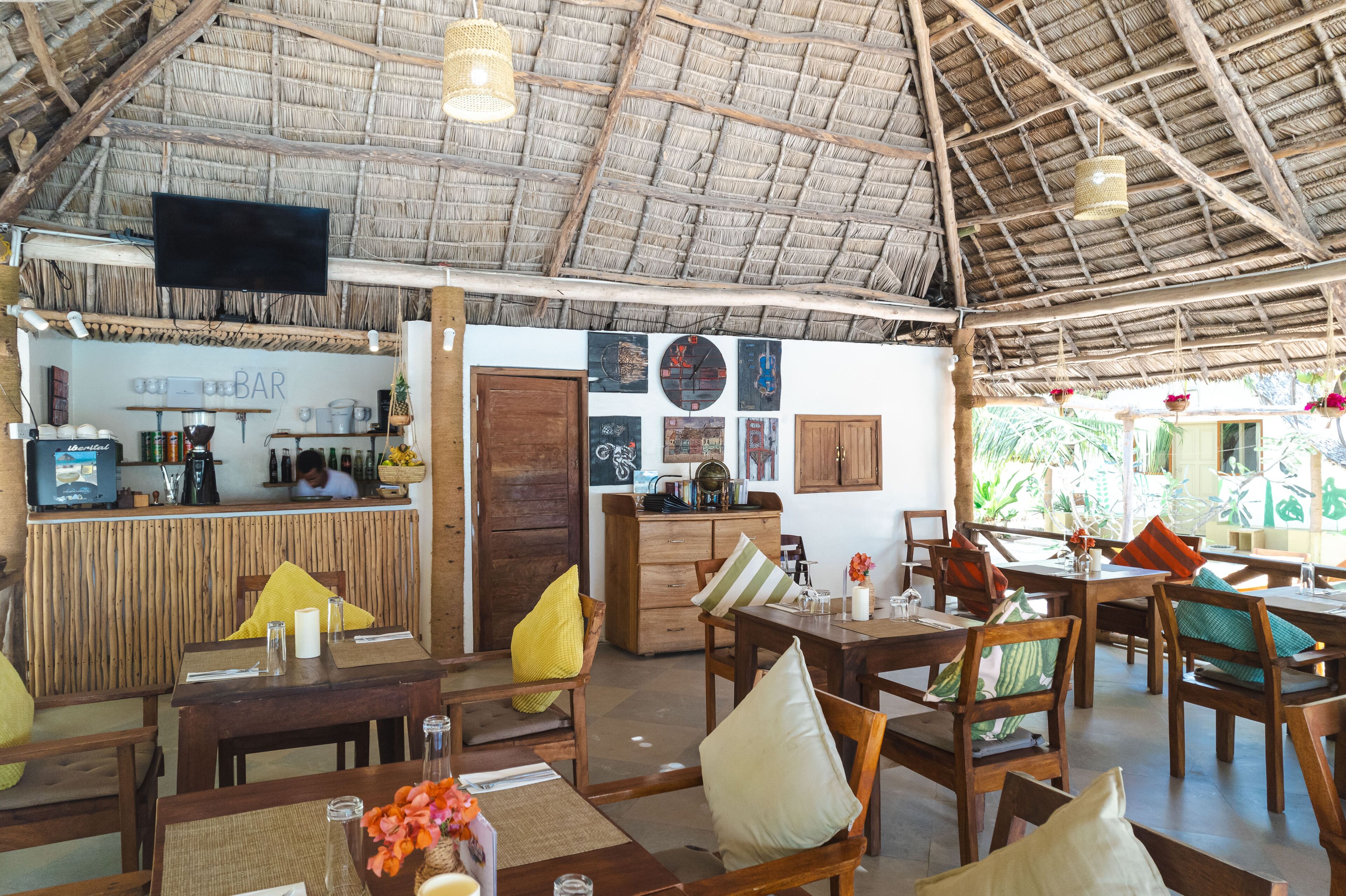 A restaurant with wooden furniture, a bar area, and a thatched roof.