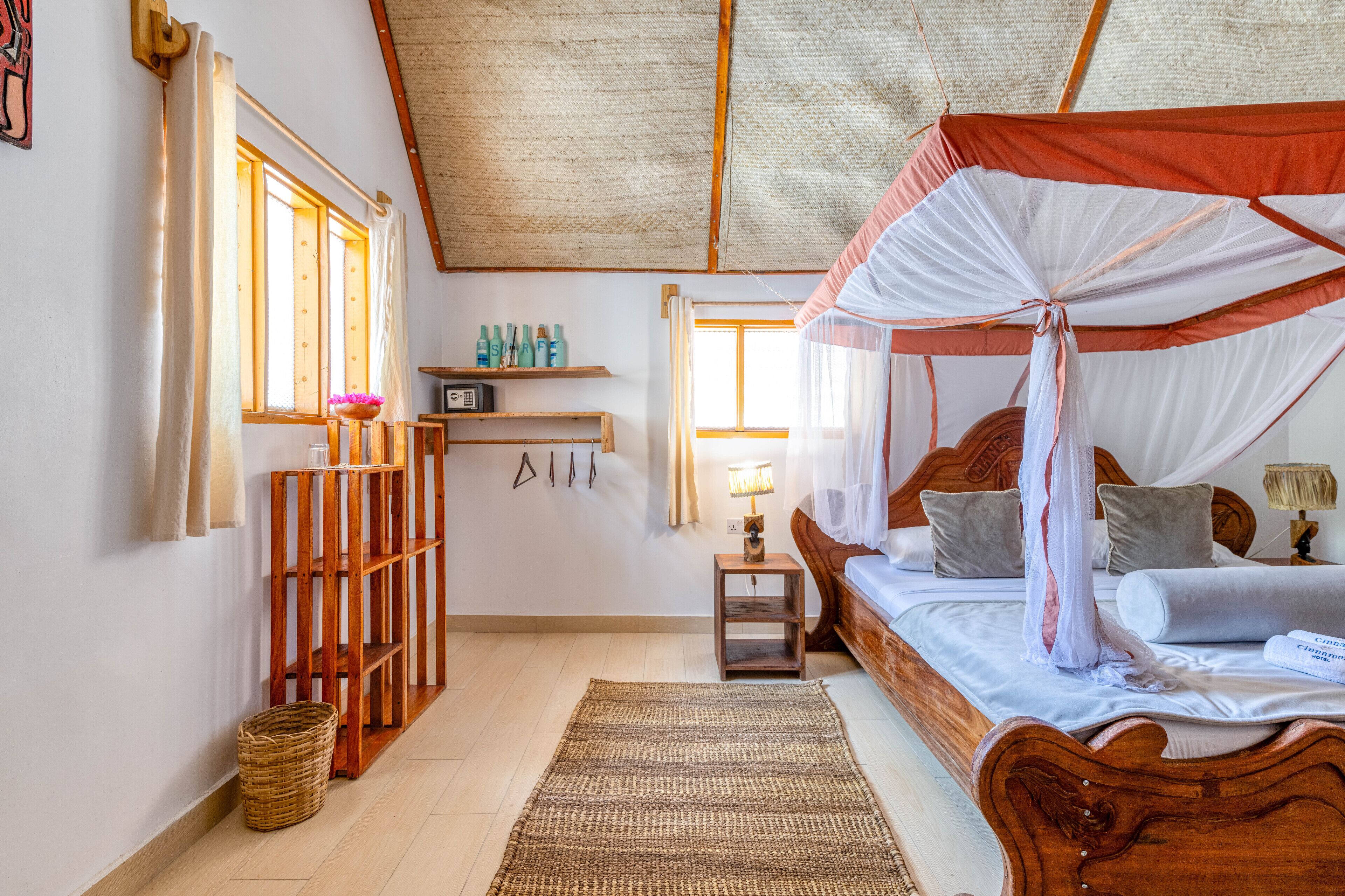 A bedroom with a wooden bed, a canopy bed, a small table with a lamp, a shelf with toiletries, and a basket on the floor.