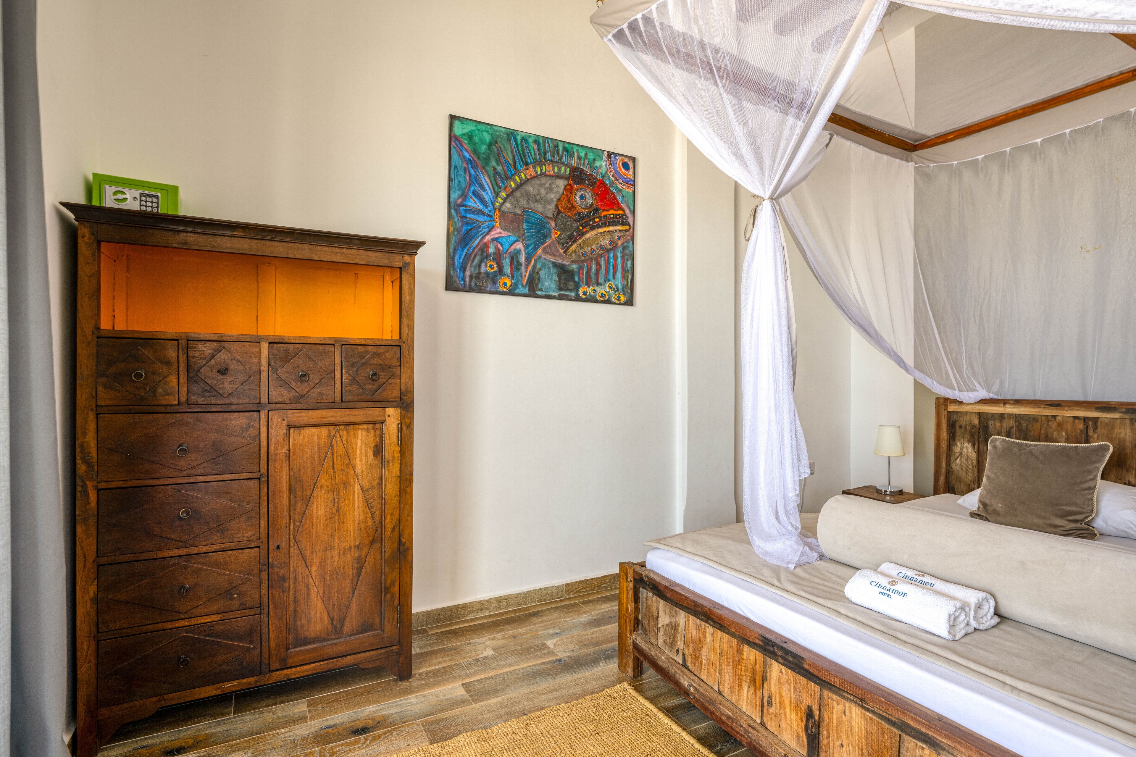 A bedroom with a wooden cabinet, a bed with a canopy, and a colorful painting on the wall.