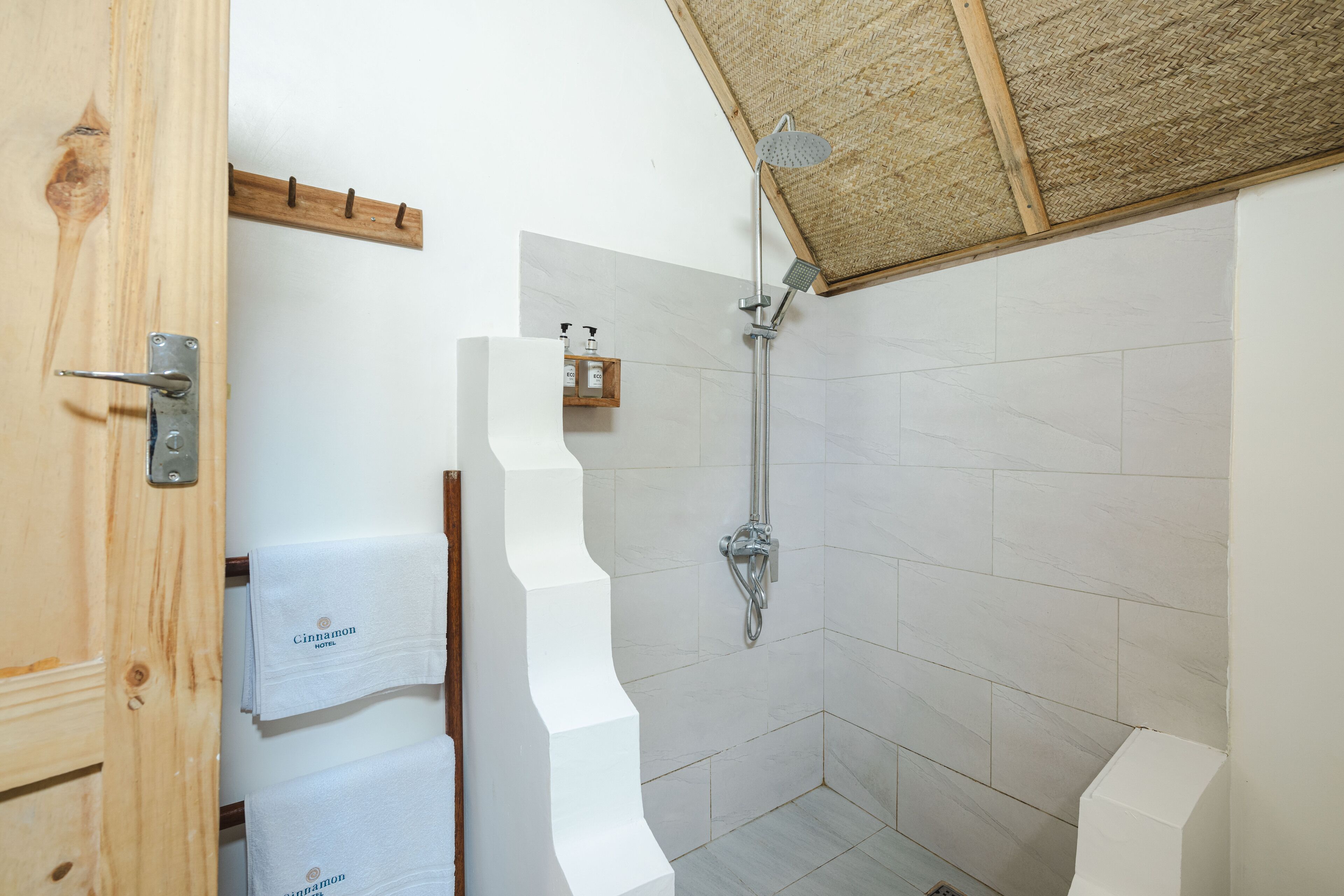 A shower with a wooden ceiling, white tiled walls, and a wooden door with a metal handle.