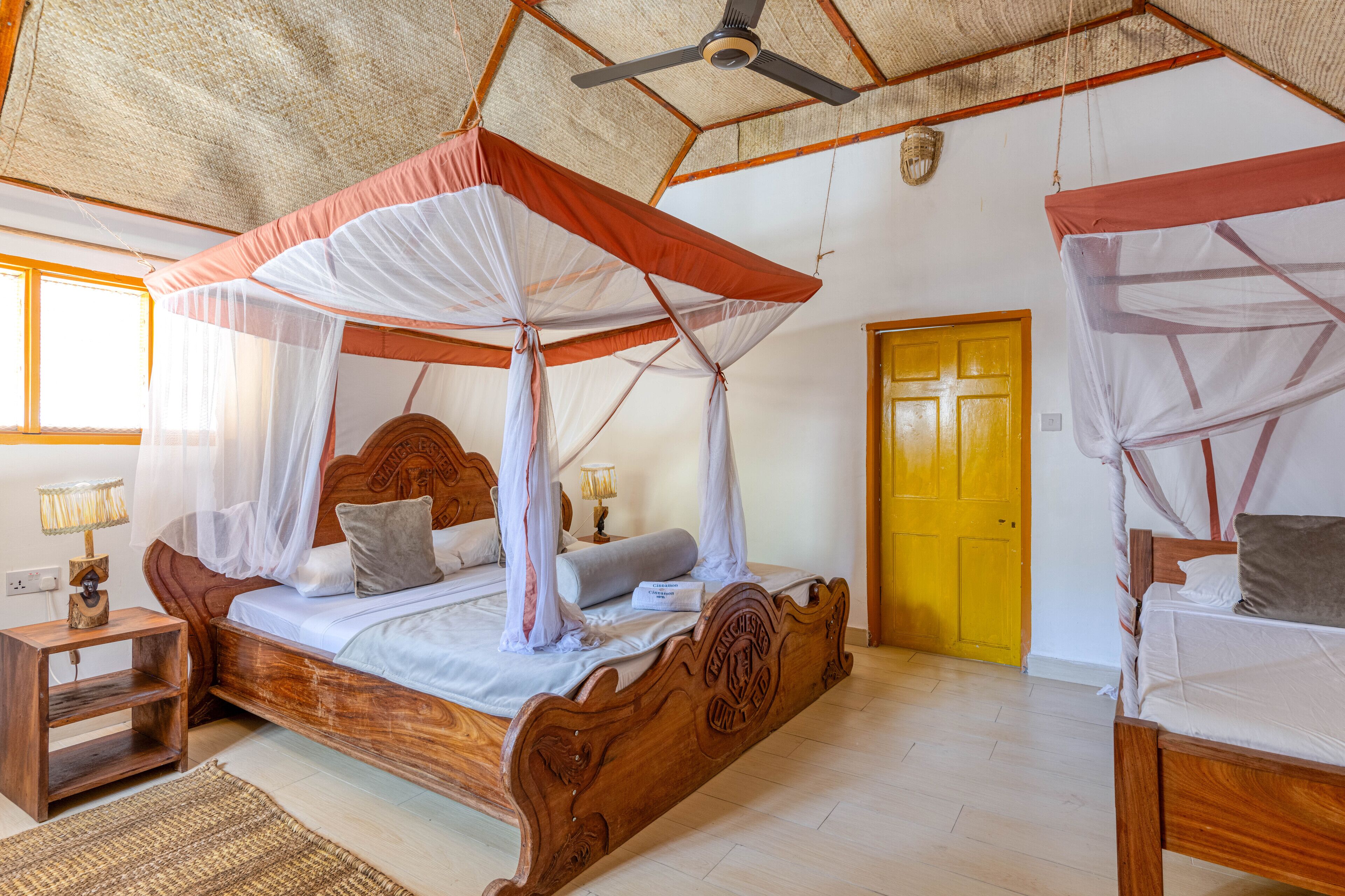 A bedroom with a wooden bed, a nightstand, a bedside table, a ceiling fan, and a yellow door.