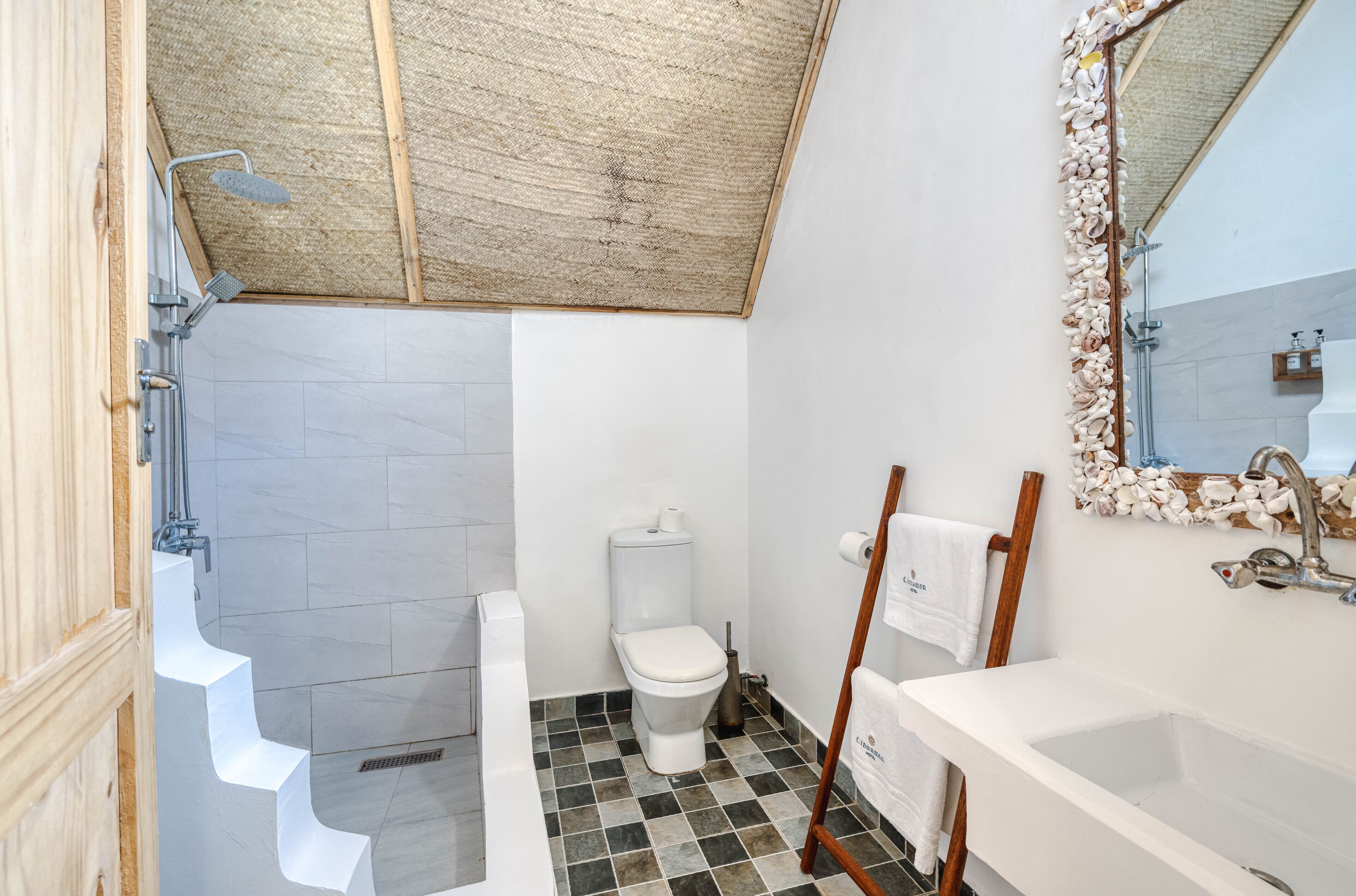 Ein Badezimmer mit Toilette, Dusche, Waschbecken und einem Spiegel mit dekorativem Rahmen.