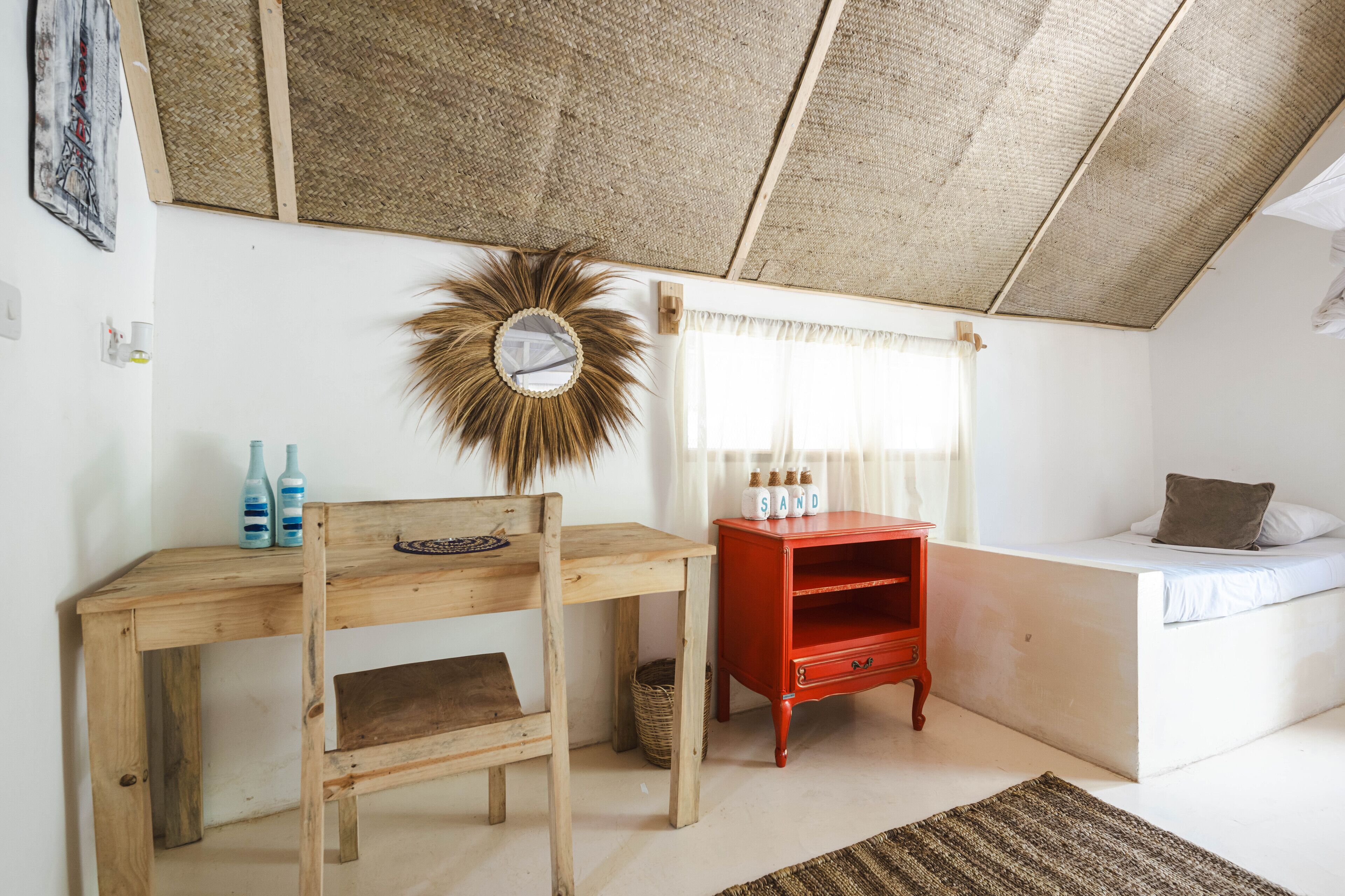 A room with a wooden desk, a red cabinet, a bed, and a large mirror on the wall.