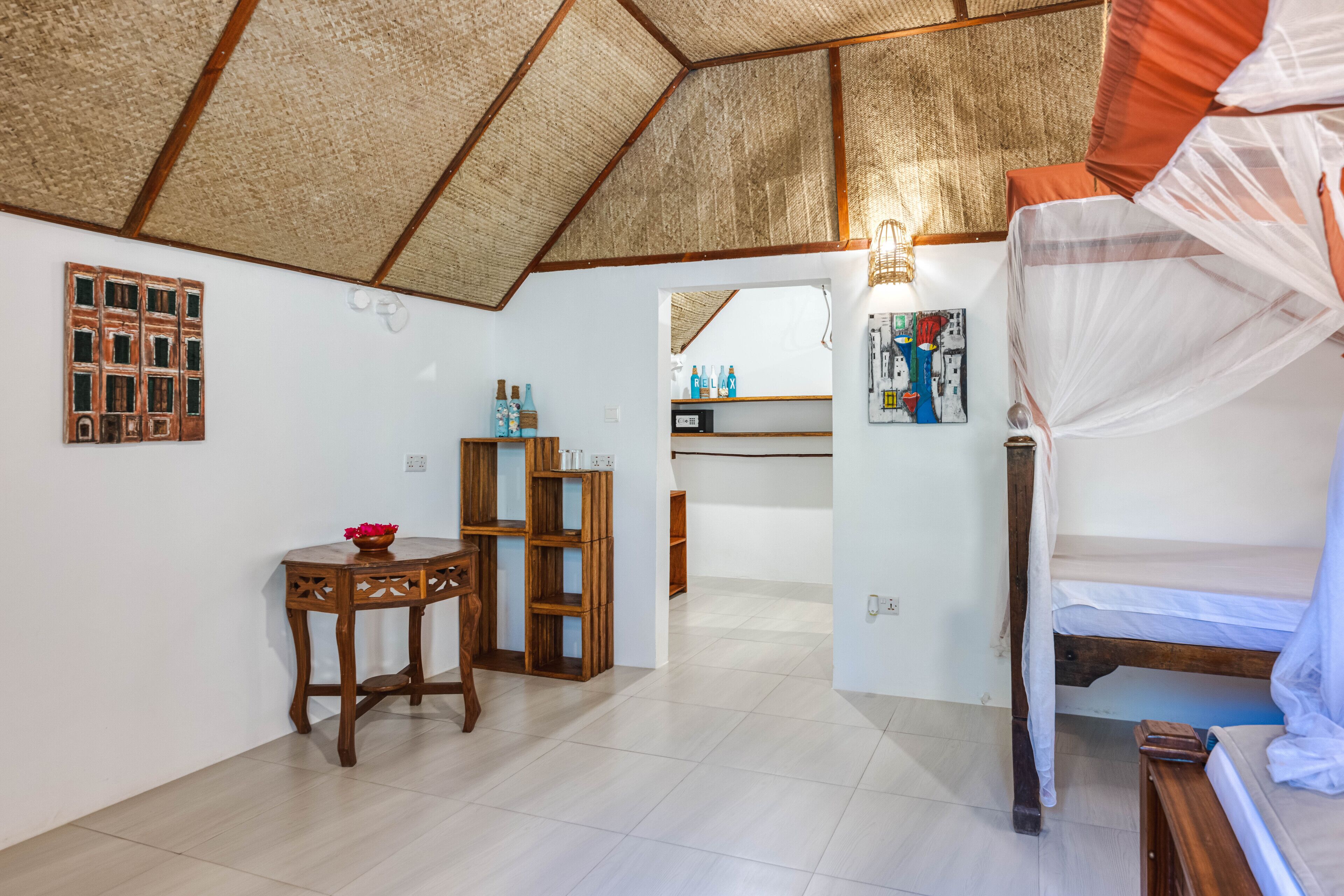 A bedroom with a bed, a small table, a shelf with bottles, and a wooden cabinet.