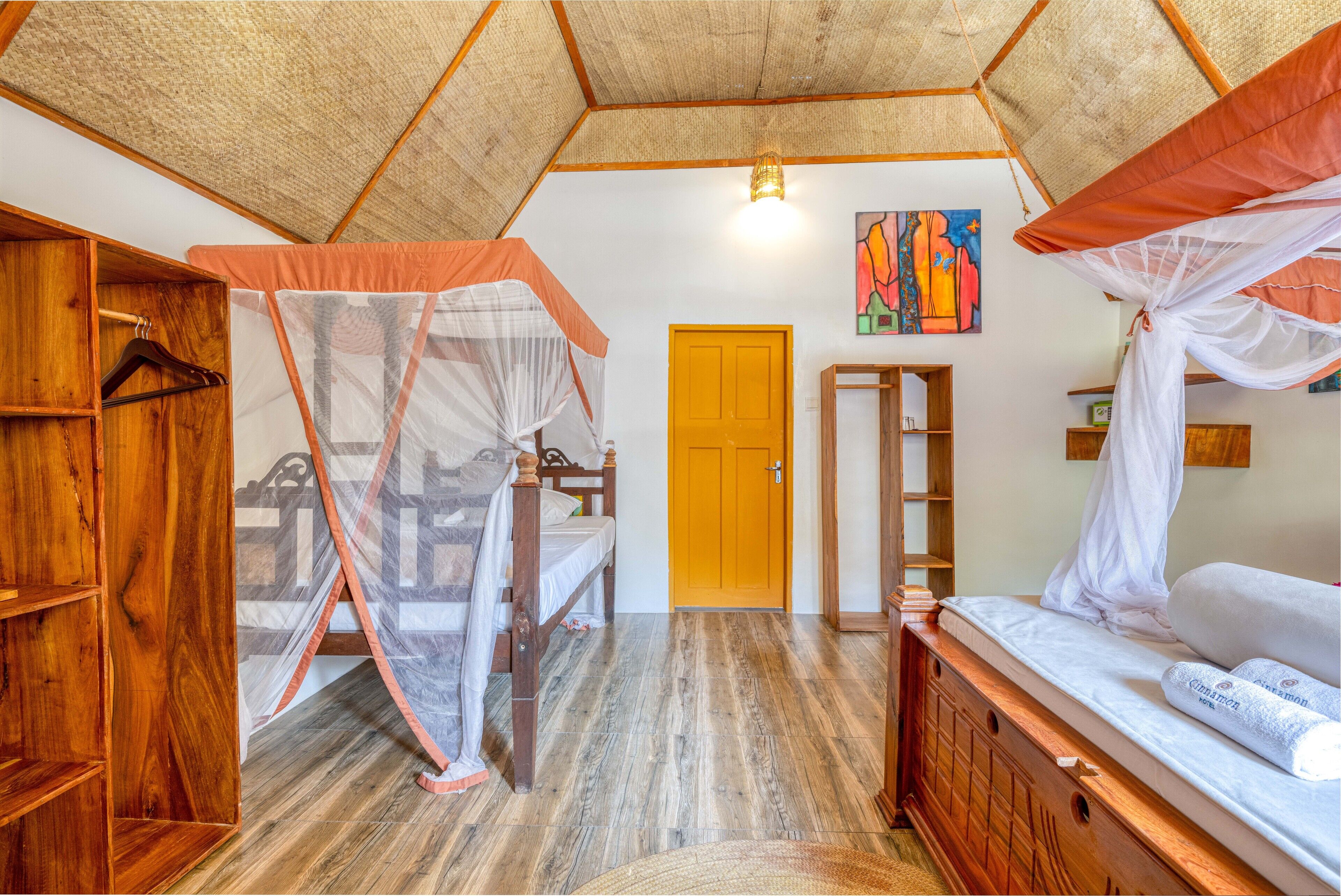 Una stanza con un letto coperto da una zanzariera, un armadio in legno, un mobiletto in legno e una porta gialla.