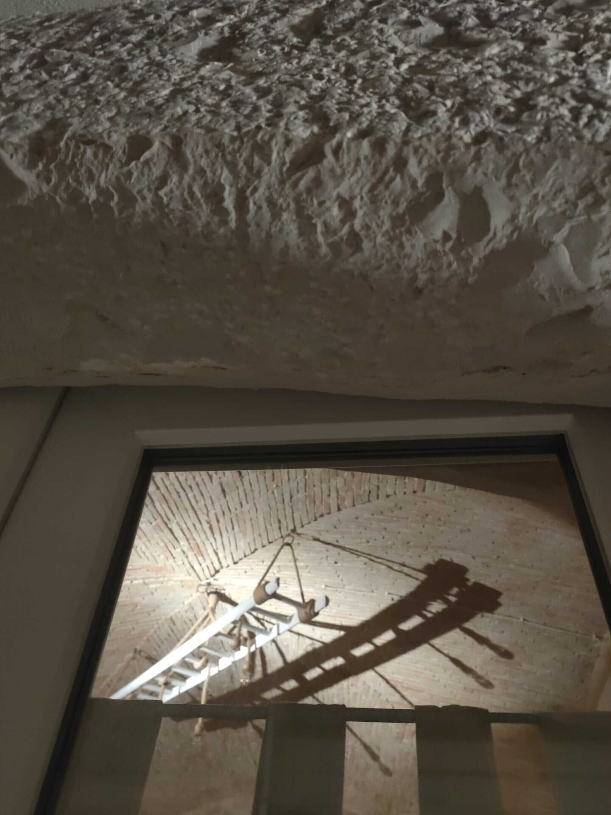 Eine Decke mit einem strukturierten Muster und ein Fenster mit Blick auf eine Holzkonstruktion.