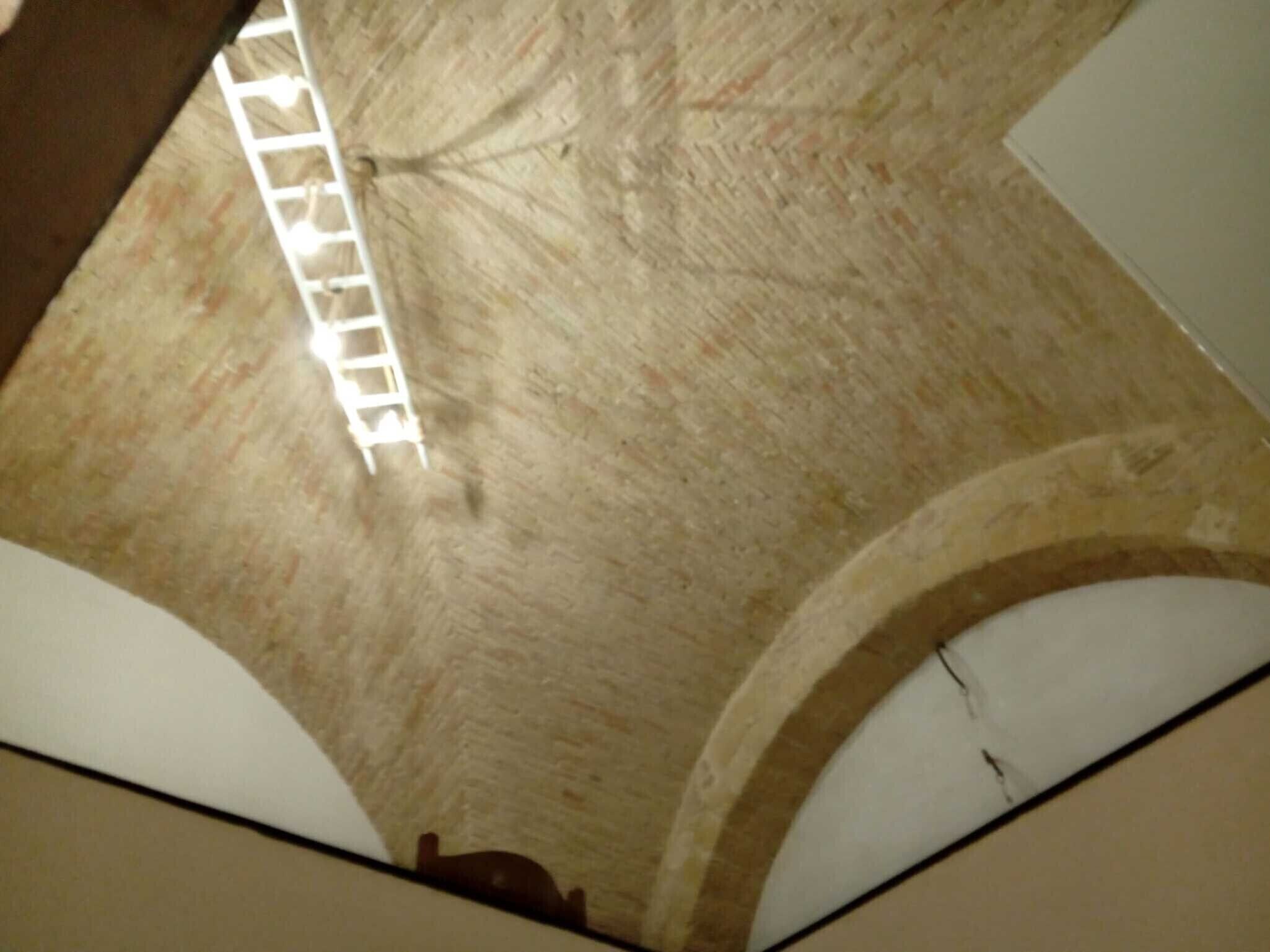 Een hoge plafond met een witte ladder, boogvormige nissen en een zichtbare constructiedraagbalk.