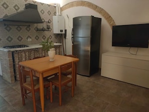 Une cuisine compacte équipée d’une cuisinière à gaz, d’un réfrigérateur en acier inoxydable, d’un téléviseur fixé au mur et d’une table à manger avec des chaises.
