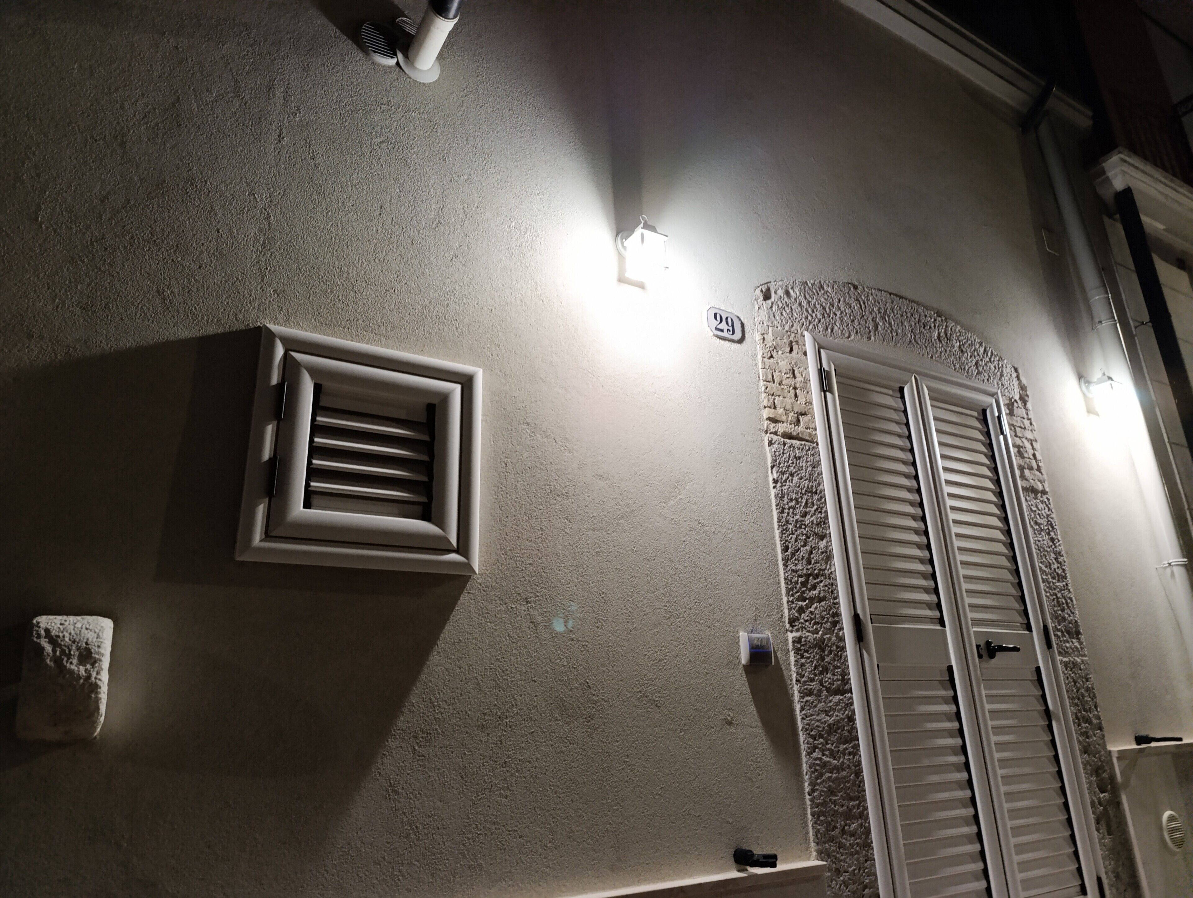 Une pièce avec une grille d’aération, un symbole « # », une fenêtre avec des volets et un luminaire fixé au mur.